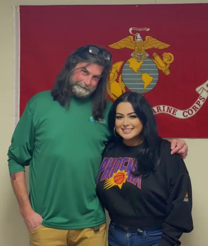 Two people posing happily in front of a Marine Corps flag indoors.