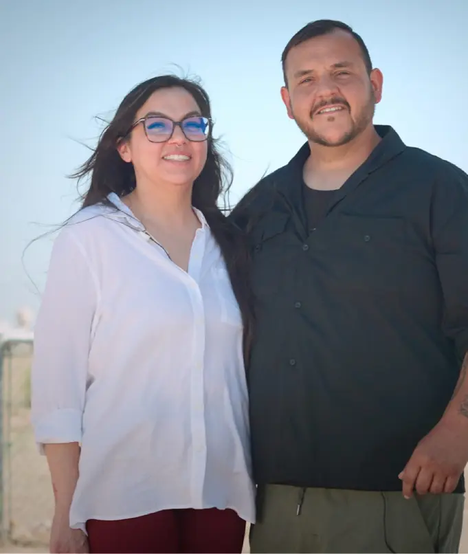 A smiling couple posing outdoors under clear blue sky.